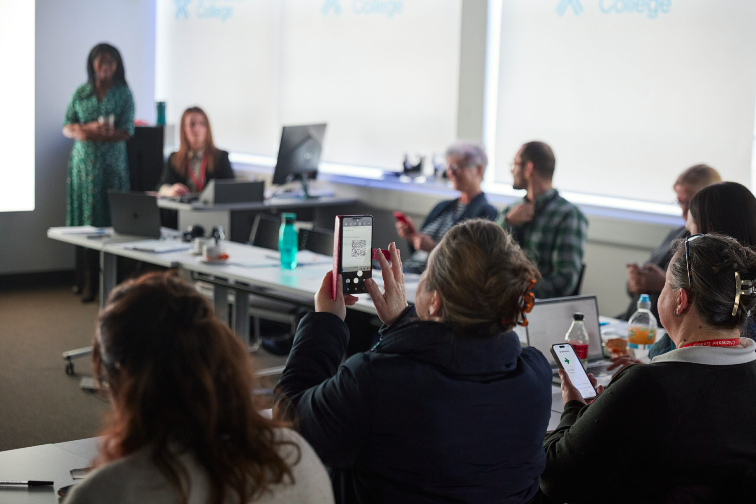 A woman scans a QR code with her phone in a classroom.